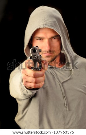 A young white, italian, male holds a semi automatic pistol during this dark photo shoot against black