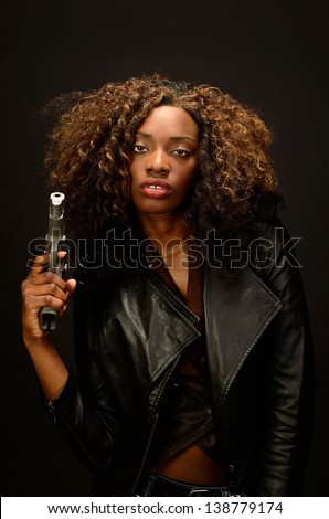 A young beautiful african american female holds a semi automatic pistol during this dark photo shoot against black