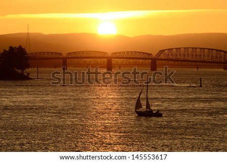 Small sailboat tacking back into port on the Columbia River near Portland Oregon at sunset with Interstate 5 bridge in background