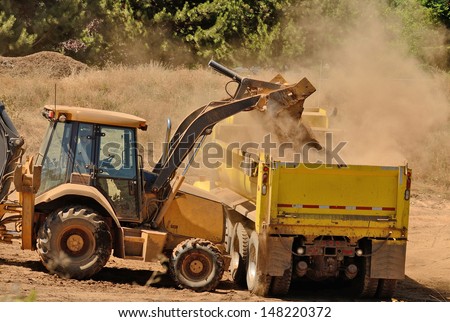 A backhoe loads duff and top soil into a 10-yard dump truck at a new commercial road development