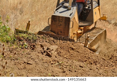 Small bulldozer moves dirt and brush at a new commercial construction development project