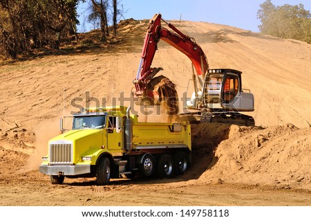 Track hoe excavator  loading a 10-yard dump truck with dirt from a new commercial development construction project.