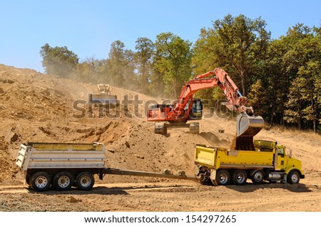 Large track hoe excavator filling a dump truck with rock and soil for fill at a new commercial development road construction project