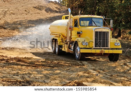 A water truck sprays water on a fresh fill layer of soil and rock for a new road construction project.