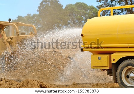 A water truck sprays water on a fresh fill layer as a large bulldozer spreads soil and rock for a new road construction project.