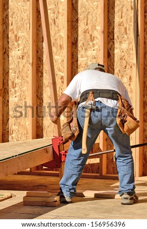 Building contractor worker using a wall jack to raise a wall for the first floor on a new home construction project
