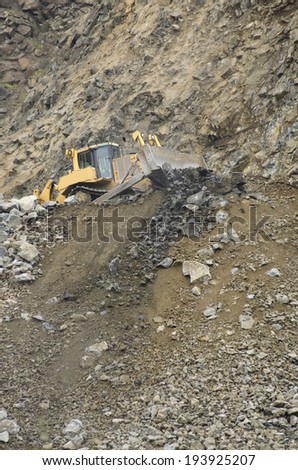 Large bulldozer moving large rocks to feed a rock crusher at a rock pit for gravel
