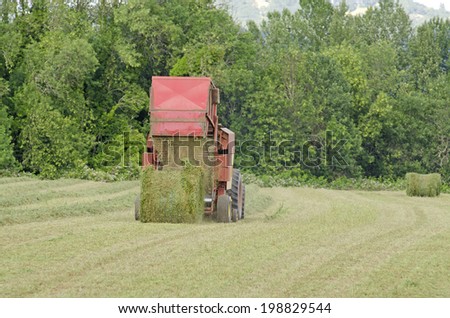 Tractor pulling a large round baler to pick up high value alfalfa grass feed from a summer field in Oregon
