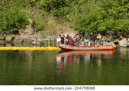 ROSEBURG, USA, USA - JUNE 02, 2014: Roseburg Hazardous materials team use a Douglas County Sheriff boat to deploy a floating oil containment boom on the Umpqua River following an vehicle accident
