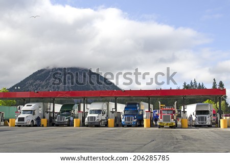 Several large over the road semi-trucks fuel up at a fueling station truck stop in California