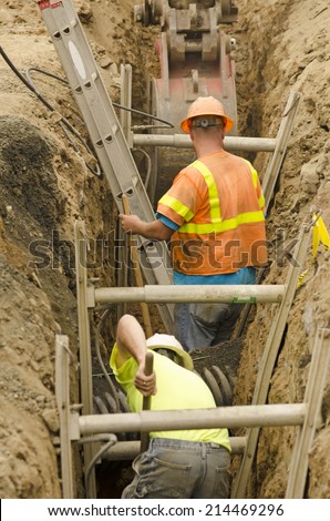 Construction workers using trench shoring equipment to backfill and install deep utilities at a new commercial  development