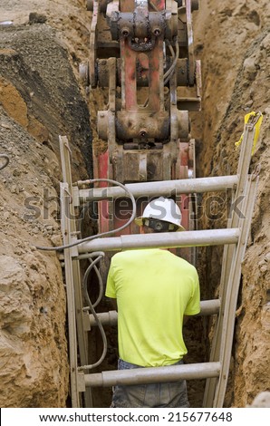 Construction workers using trench shoring equipment to backfill and install deep utilities at a new commercial  development