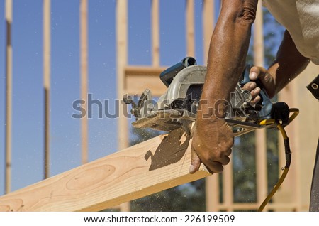 Building contractor worker using hand held worm drive circular saw to cut boards on a new home construction project
