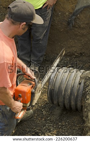 Excavation contractor uses a chain saw to cut plastic drain pipe for a new commercial street storm drain sewer