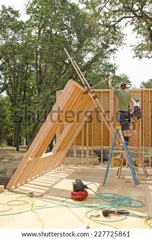 Building contractor worker using a wall jack to raise a wood stud wall on a new home construction project