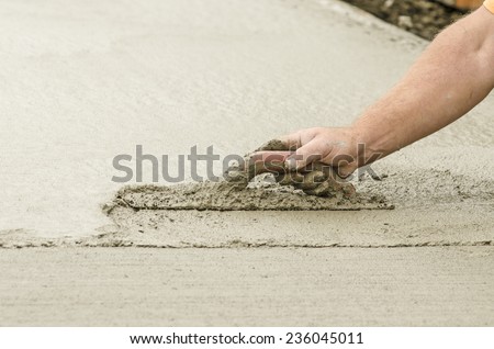 Concrete construction contractor using a trowel to smooth a sidewalk, curb and storm drainage gutter on a new urban road street project