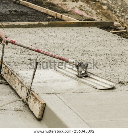 Concrete construction contractor using a float to  smooth a sidewalk, curb and storm drainage gutter on a new urban road street project