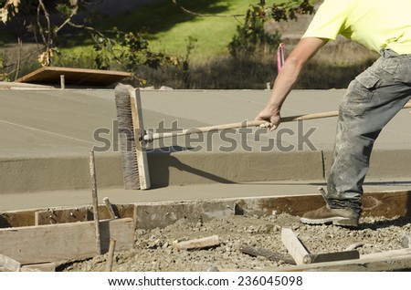 Concrete construction contractor using a broom to install texture in a sidewalk, curb and storm drainage gutter on a new urban road street project