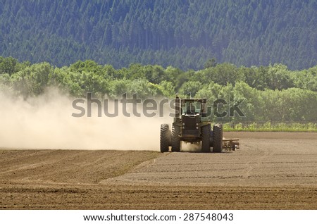 Large agricultural tractor smoothing out a tilled field with a disc implement preparing for planting