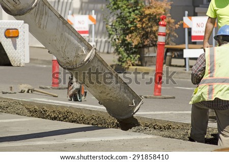 Construction workers installing new utilities pour concrete to cover and stabilize a trench with water and sewer pipe
