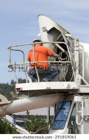 Cement mixer truck driver cleaning up concrete from chute following a delivery on a new road construction project