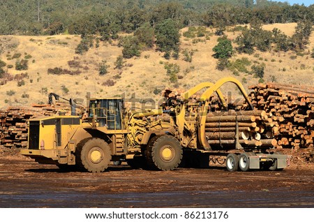 A large wheeled loader unloads a log truck at a small log sawmill in Oregon