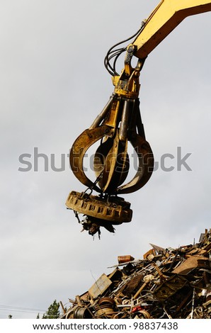 Large tracked excavator working a steel pile at a metal recycle yard with a magnet.