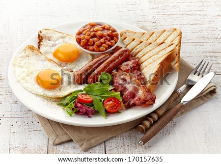 English breakfast with fried eggs, bacon, sausages, beans, toasts and fresh salad