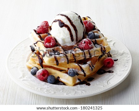 Plate of belgian waffles with ice cream, chocolate sauce and fresh berries