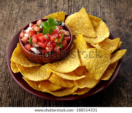 Plate of nachos and fresh salsa dip on wooden background