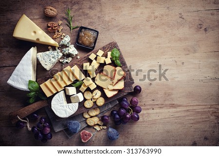 Cheese plate served with grapes, jam, figs, crackers and nuts on a wooden background