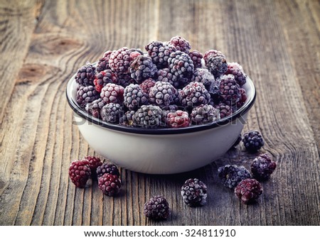 Frozen blackberries in a white bowl on wooden background