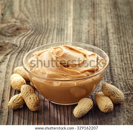 Bowl of peanut butter and peanuts on wooden background