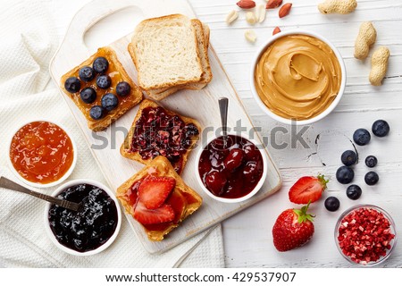 Sandwiches with peanut butter, jam and fresh fruits on white wooden background from top view