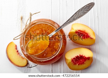 Jar of peach jam on white wooden background from top view