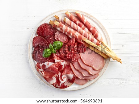 Cold smoked meat plate with pork chops, prosciutto, salami and bread sticks on white wooden background. From top view