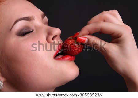 Beautiful female with red lips,biting a strawberry