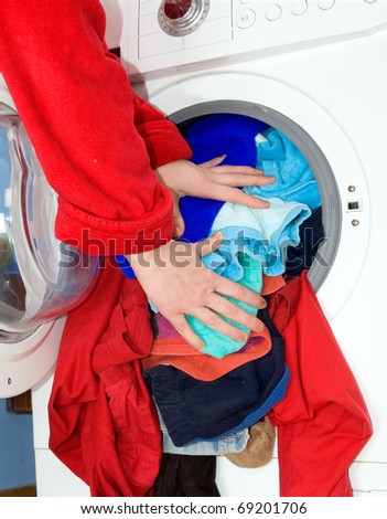 Close-up on female hand putting colorful clothes into washing machine drum