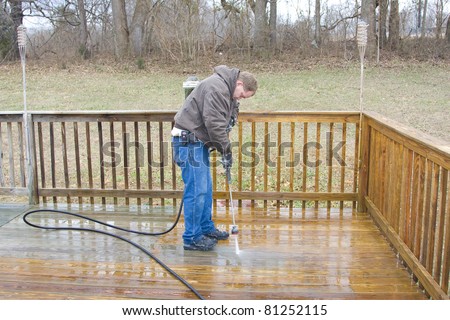 Worker pressure washing deck on rear of house