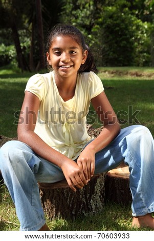 Young happy school girl outdoors sitting on logs in sunshine
