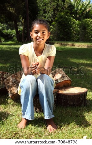 Young happy school girl outdoors sitting on logs bare footed