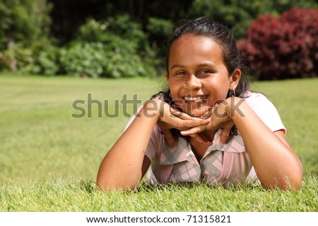 Smiling girl lying on grass chin on hands