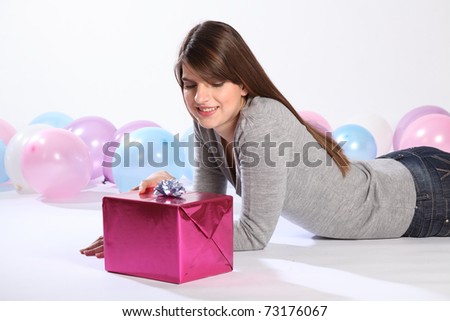 Happy birthday. Time to celebrate for beautiful young caucasian girl with long hair, smiling while lying on the floor with a birthday present.