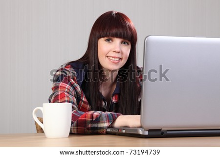 Beautiful happy young caucasian student girl at home, sitting to her desk working on laptop doing homework.