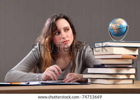 Teenage caucasian student girl at home, sitting to her desk studying the globe for geography homework with work books nearby.