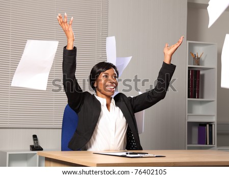 Beautiful young black woman working in office throws a load of papers into the air in happiness. She has a beautiful smile.