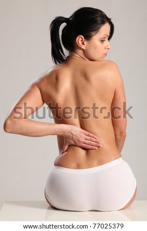 Lower back pain and ache for beautiful young woman wearing white knickers with a naked back.