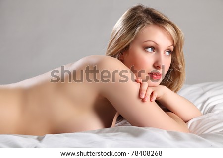 Voluptuous beautiful young blonde woman with blue eyes lying naked in bed. Picture has been retouched for air brushed look.