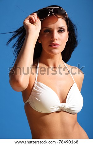 Beautiful sexy young woman wearing white bikini and sun glasses standing outdoor in the bright sunshine against a blue sky.