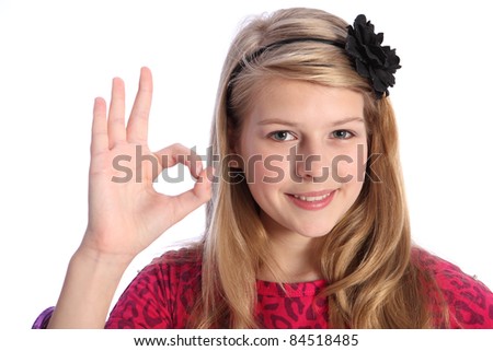 Fun positive okay hand sign by pretty caucasian school girl with happy smile, wearing pink t-shirt with black flower hair band in her blonde hair.